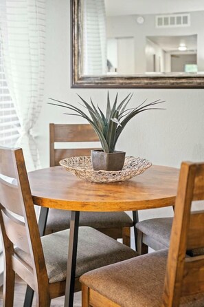 A round wooden dining table with a woven placemat, a potted plant, and four upholstered chairs. - Elegant 2BR Apartment right by Cowboys Stadium! (Arlington)
