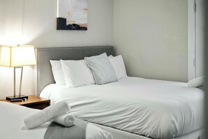 A neatly made bed with white linens and pillows, a bedside lamp, and a wall-mounted abstract painting. - Elegant 2BR Apartment right by Cowboys Stadium! (Arlington)