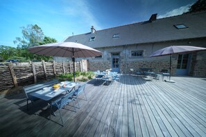 An outdoor patio with tables and chairs, umbrellas, and a stone building in the background. - The Kordokov vacation rental—a renovated old farmhouse near the sea, set in the heart of a stable (Tréméreuc)