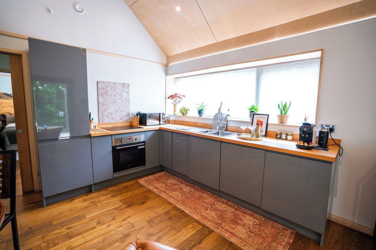 Een moderne keuken met grijze kastjes, een houten aanrechtblad en een groot raam dat voor natuurlijk licht zorgt.