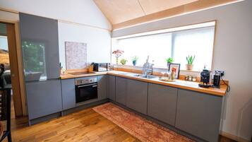 Een moderne keuken met grijze kastjes, een houten aanrechtblad en een groot raam dat voor natuurlijk licht zorgt.