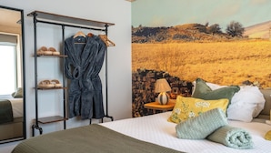 Een slaapkamer met een bed, een kledingrek, een lamp en een schilderij van een landschap.