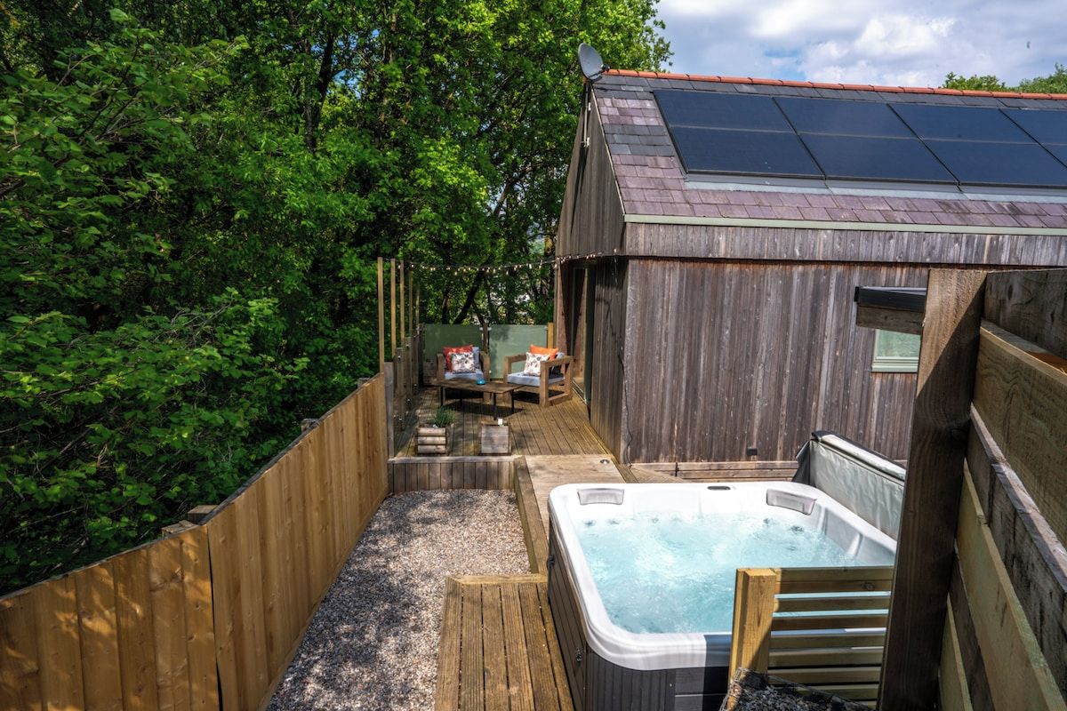 Una terraza de madera con un jacuzzi y una pequeña construcción con un panel solar.