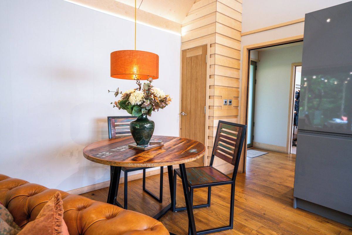 A dining area with a round table, chairs, a vase with flowers, and a hanging lamp.