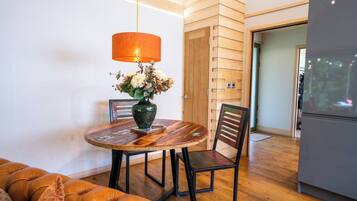 A dining area with a round table, chairs, a vase with flowers, and a hanging lamp.