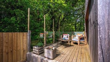 Terraza de madera con mobiliario exterior, rodeada por una valla de madera y abundante vegetación.