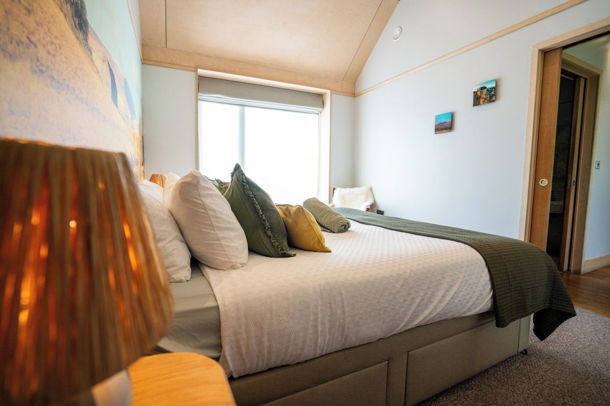 A bedroom with a bed, a window, a door, and a painting on the wall.