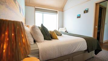 A bedroom with a bed, a window, a door, and a painting on the wall.