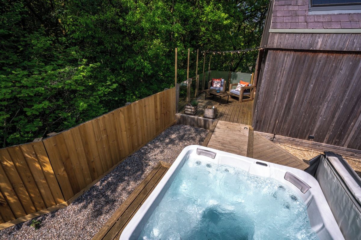 A hot tub in a backyard with a wooden deck and a wooden fence.