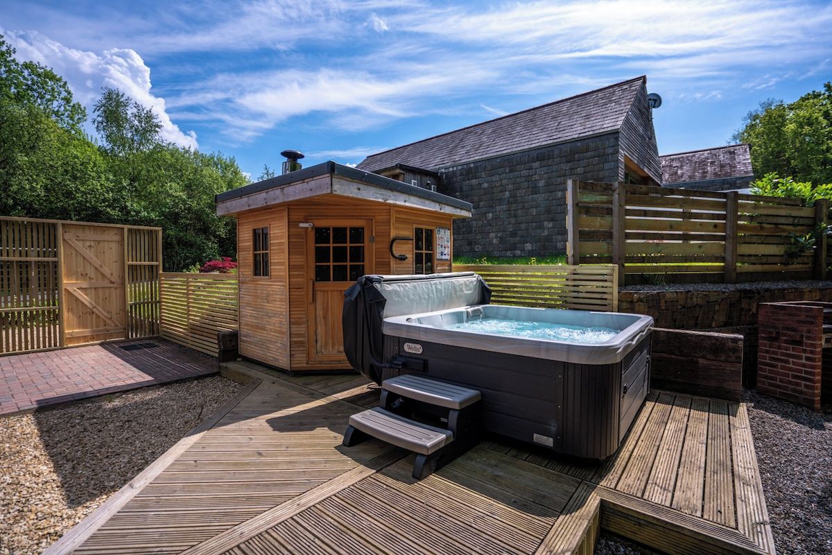 A hot tub and wooden cabin in a backyard with a wooden deck and a brick wall.