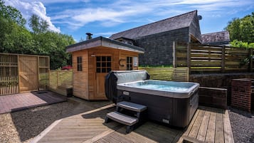 A hot tub and wooden cabin in a backyard with a wooden deck and a brick wall.