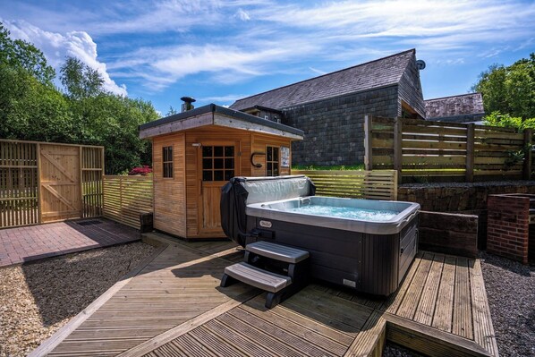 A hot tub and wooden cabin in a backyard with a wooden deck and a brick wall.