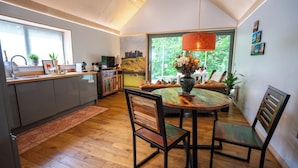 Een moderne keuken met een eethoek, houten vloeren en een groot raam dat natuurlijk licht binnenlaat.