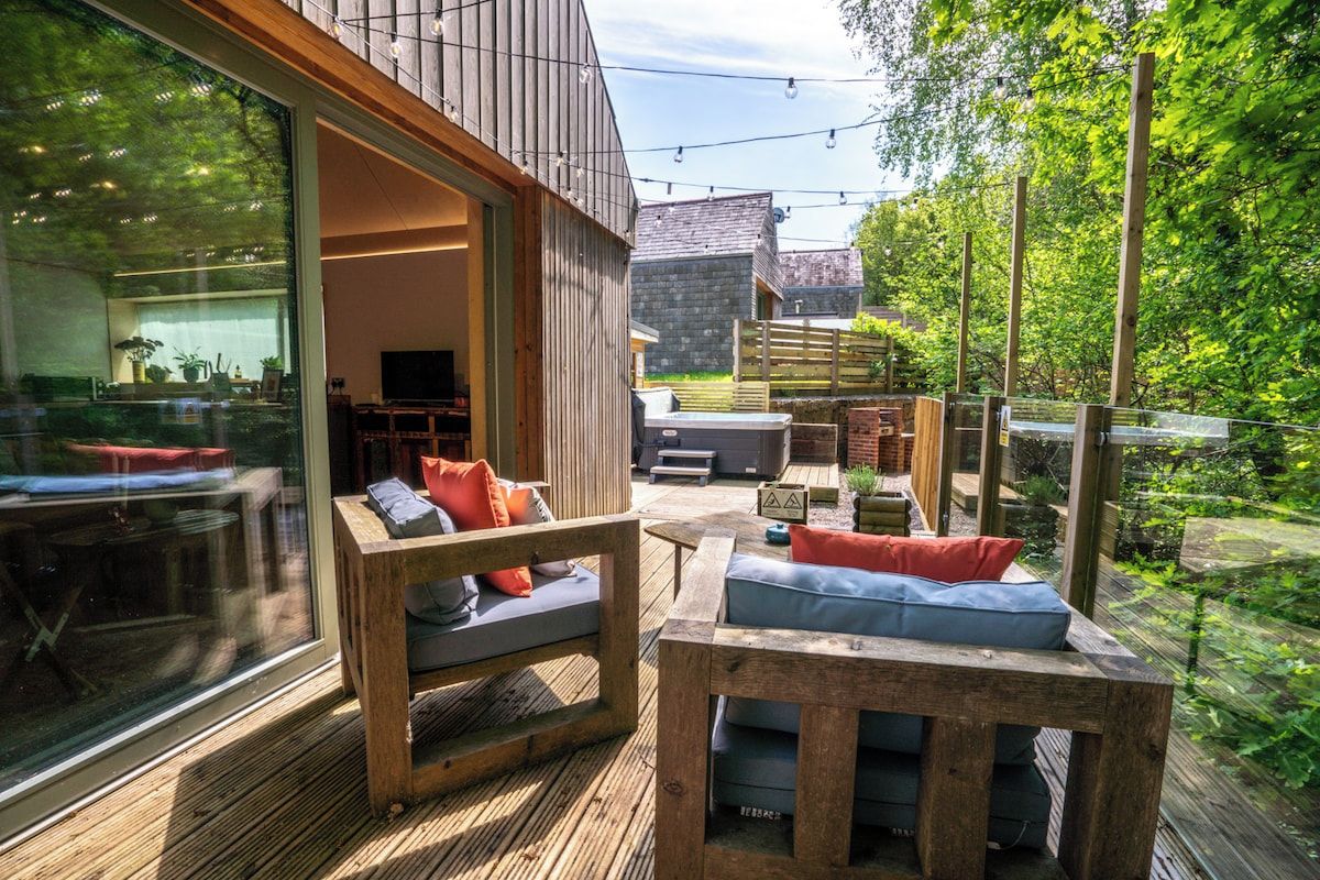 An outdoor seating area with wooden furniture and a glass wall overlooking a garden.