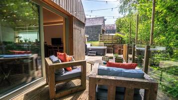An outdoor seating area with wooden furniture and a glass wall overlooking a garden.