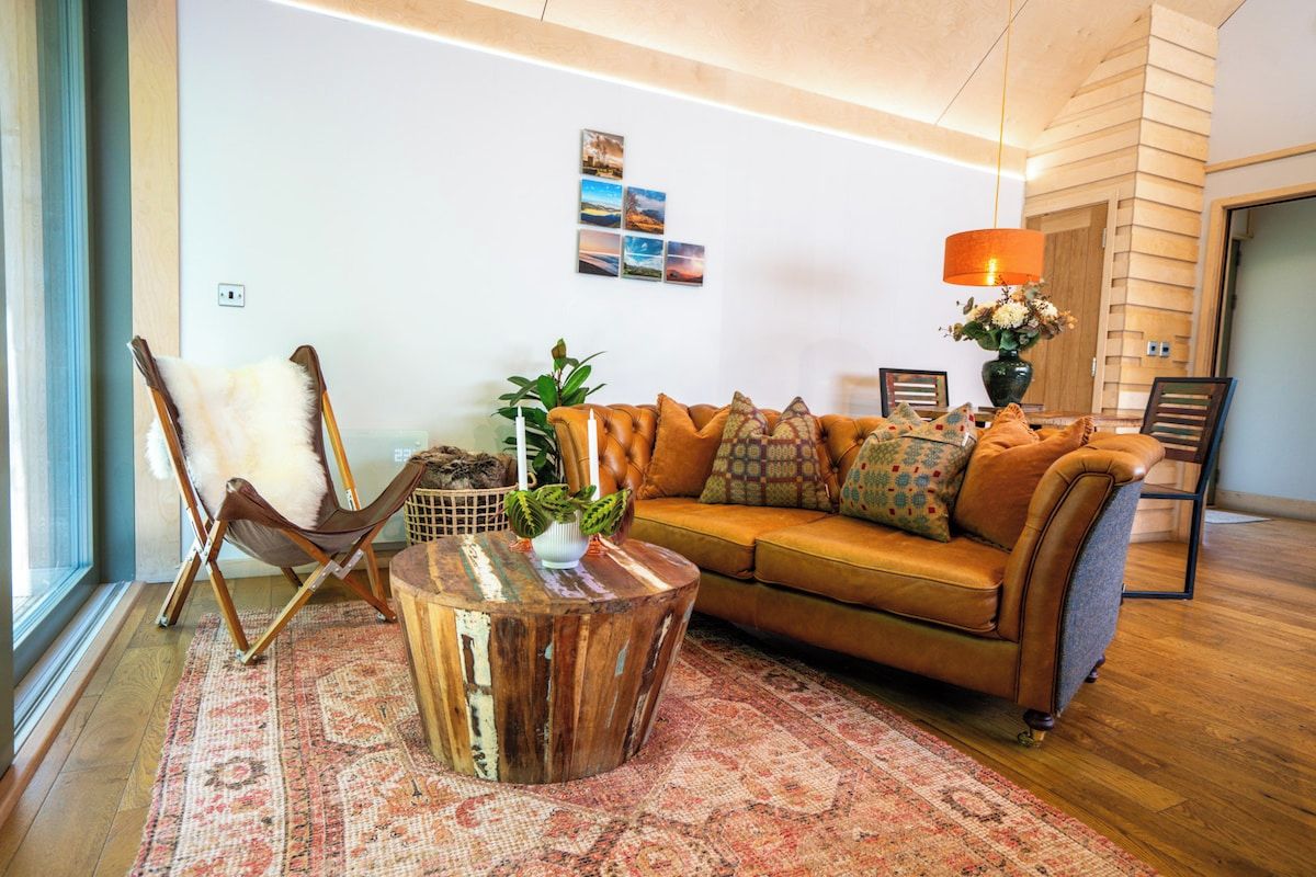 A living room with a leather sofa, a wooden coffee table, a patterned rug, a chair, and a wall with a picture.