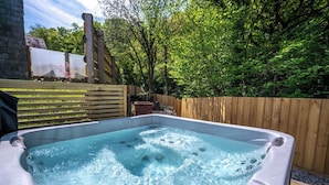 Een hottub in een open omgeving, met een houten omheining en bomen op de achtergrond.