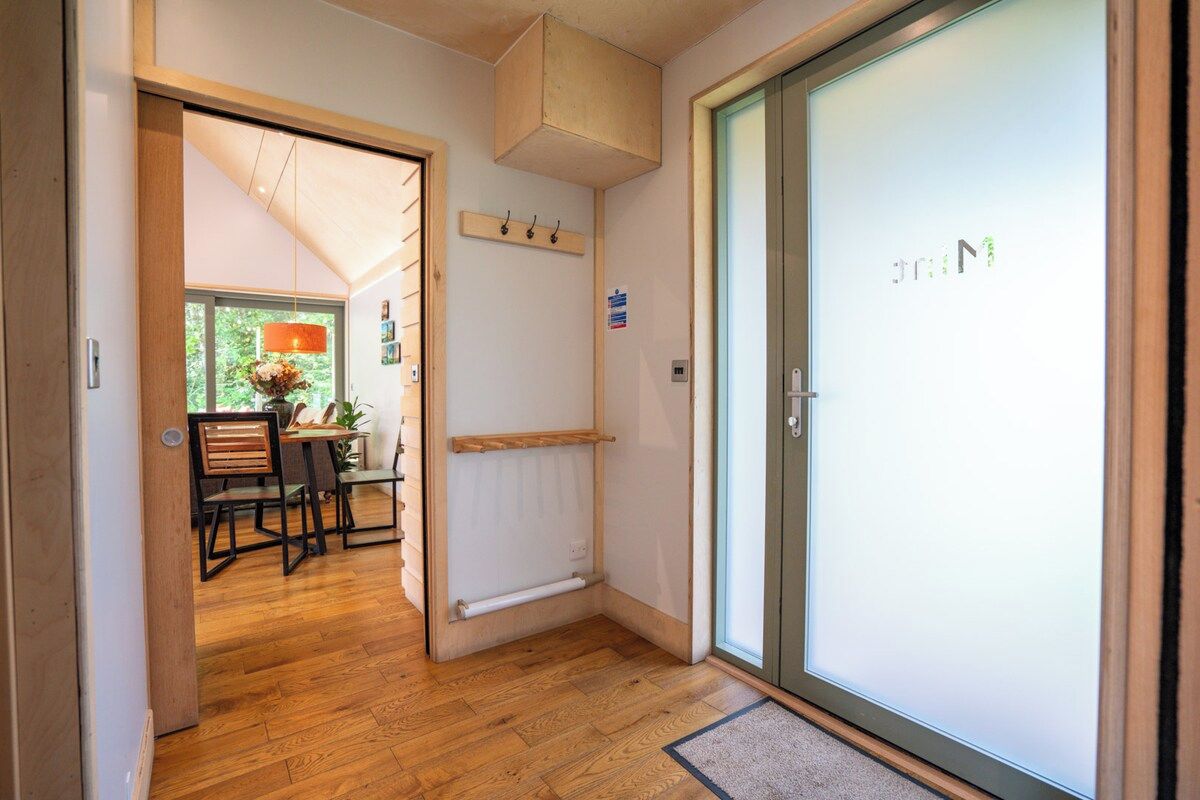 A hallway with a wooden floor, a dining area with a table and chairs, a radiator, and a door with a frosted glass panel.