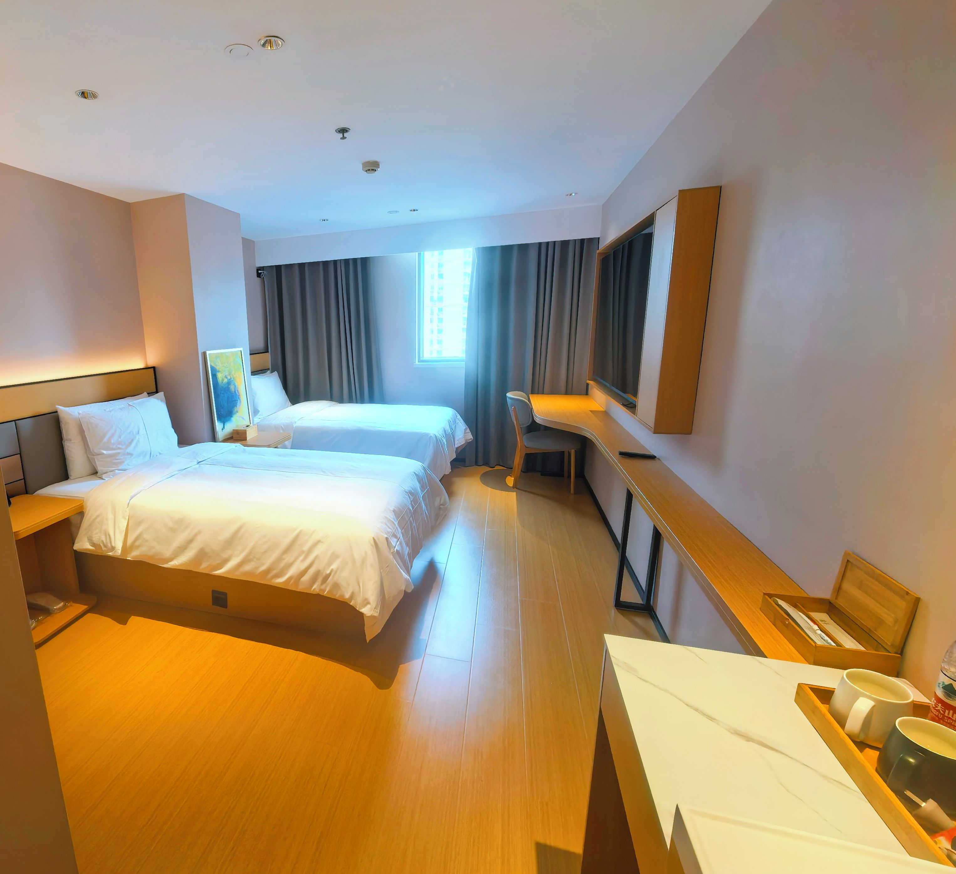 A hotel room with two beds, a desk, a chair, a TV, and a window.