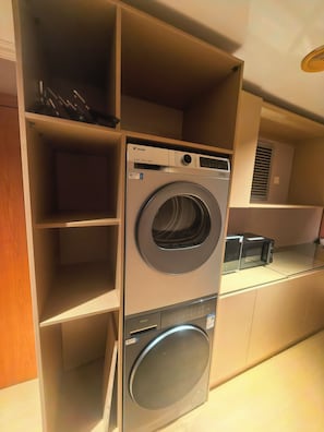 Un espace buanderie compact comprenant un lave-linge et un sèche-linge à chargement frontal, des étagères intégrées et un four à micro-ondes posé sur le plan de travail.