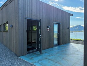 A modern building with a wooden exterior, a glass door, and a view of a lake and mountains. - Artist's home with studio in the heart of Lofoten (Nordland)
