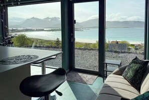 A modern interior with a sofa, a dining table, and a view of a beach and mountains. - Artist's home with studio in the heart of Lofoten (Nordland)