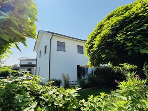 A modern two-story house with a white exterior, surrounded by lush greenery and a well-maintained garden. - Claudia's Seeherz (Wasserburg am Bodensee)