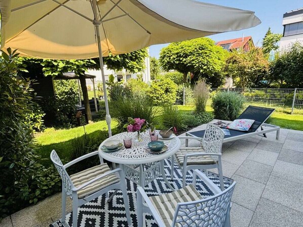 An outdoor patio with a round table, chairs, and a sun umbrella. - Claudia's Seeherz (Wasserburg am Bodensee)