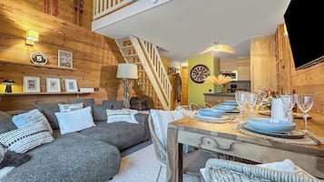 A cozy room with a sofa, a dining table set with plates and glasses, a staircase, and wooden walls.