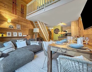 Ein gemütliches Zimmer mit einer Couch, einem Esstisch gedeckt mit Tellern und Gläsern, einer Treppe und Holzwänden.