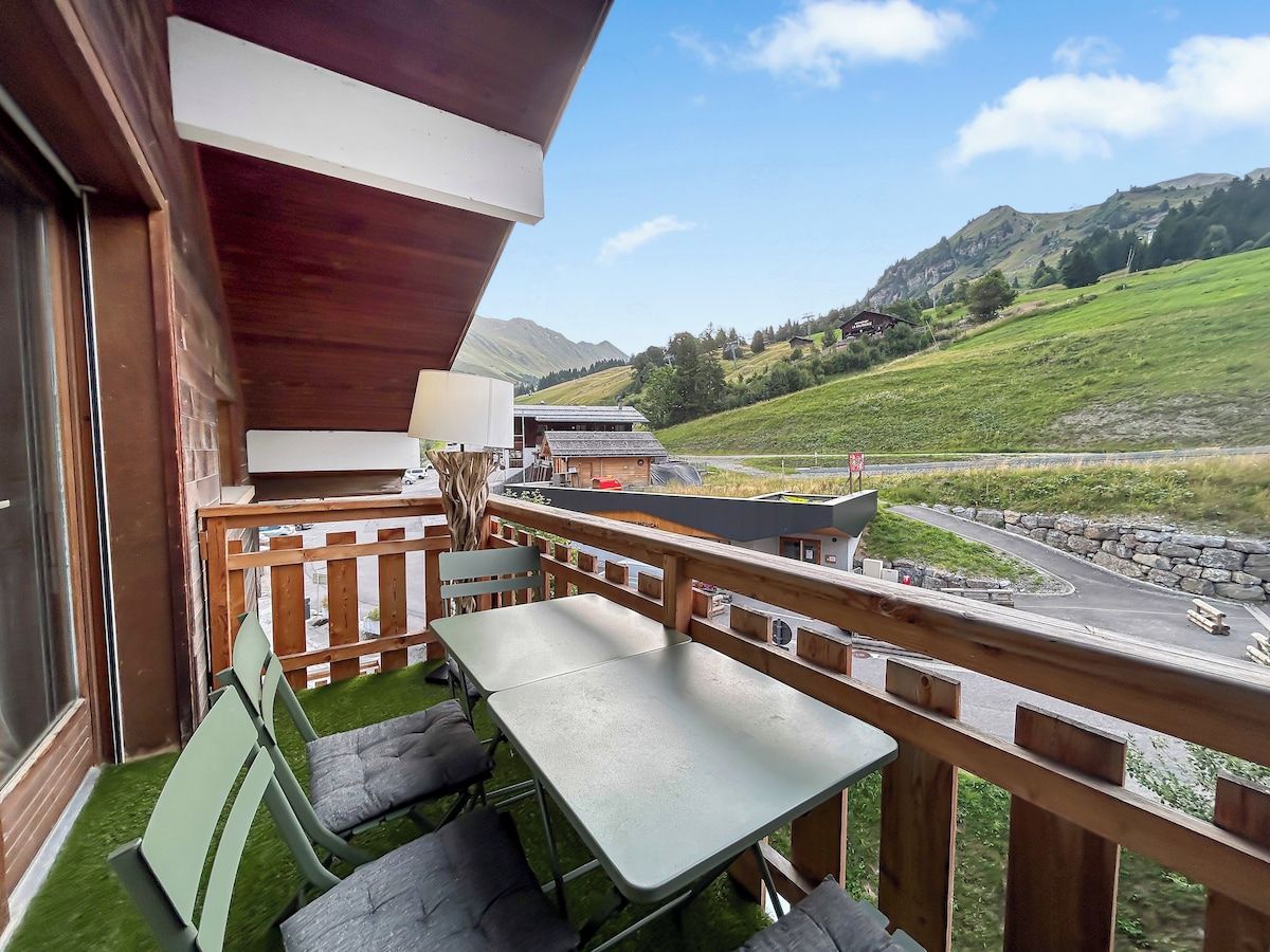 A wooden deck with a table and chairs, overlooking a road and green hills.