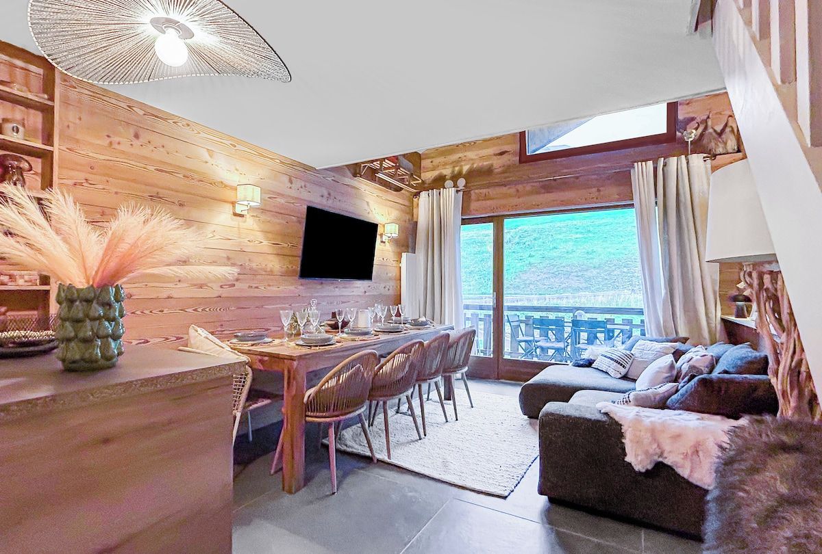 Een houten interieur met een eethoek, een bank en een groot raam met uitzicht op een wateroppervlak.