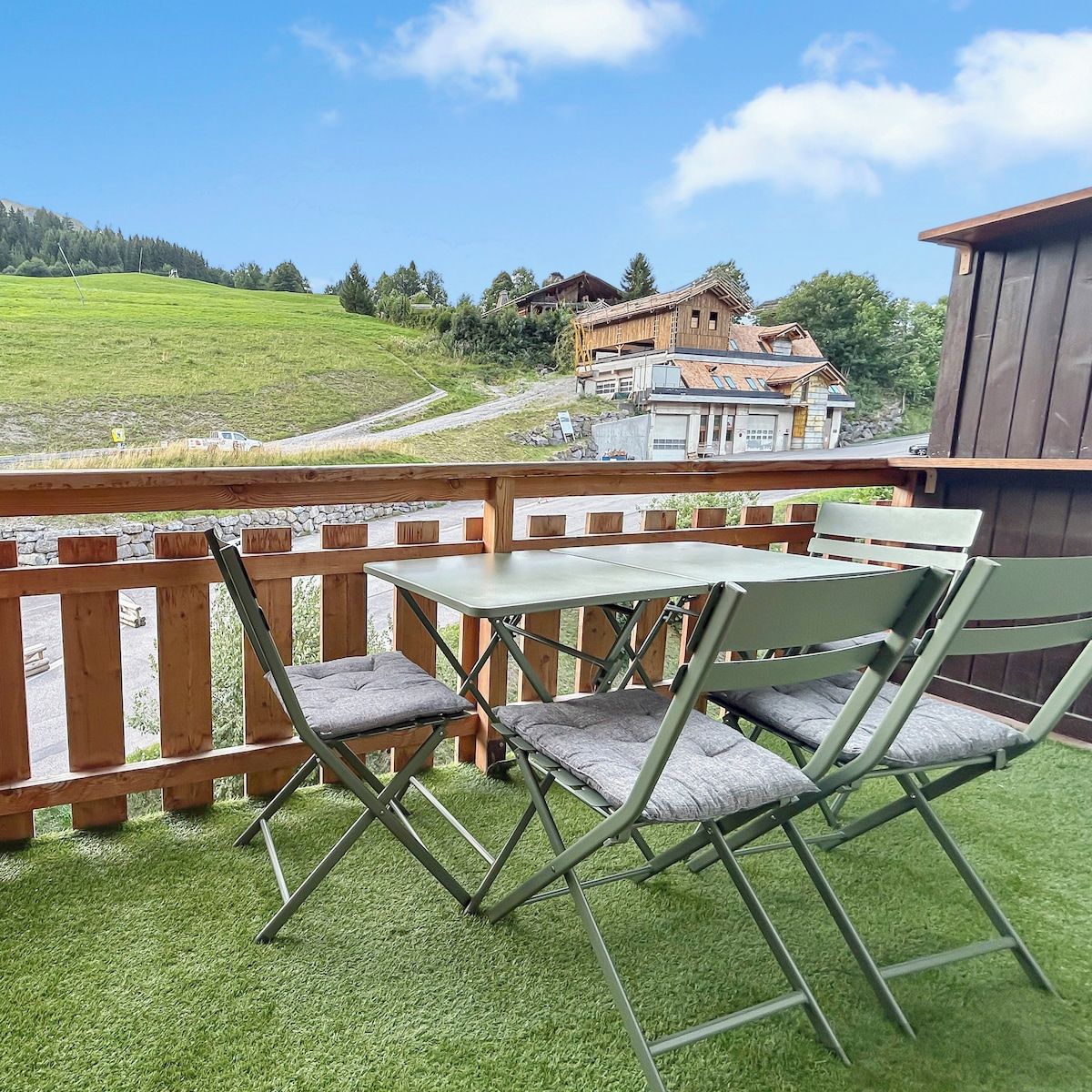 Ein Balkon mit Tisch und Stühlen, der auf eine grüne Landschaft und Gebäude in der Ferne blickt.