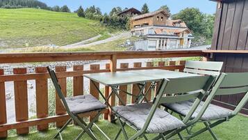 Ein Balkon mit Tisch und Stühlen, der auf eine grüne Landschaft und Gebäude in der Ferne blickt.