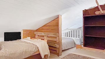 A bedroom with a sloped ceiling, a wooden headboard, a bed with a white comforter, a wooden dresser, and a white railing.