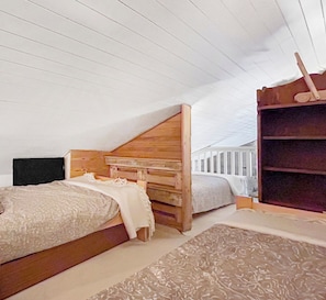 Ein Schlafzimmer mit schrägem Dach, einem Holzkopfteil, einem Bett mit weißer Bettdecke, einer Holzkammer und einem weißen Geländer.