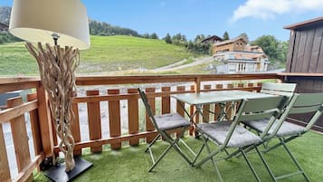 Een balkon met een tafel, stoelen, een lamp en uitzicht op een groen landschap en gebouwen.