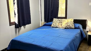 A bedroom with a bed, curtains, a window, and a nightstand.