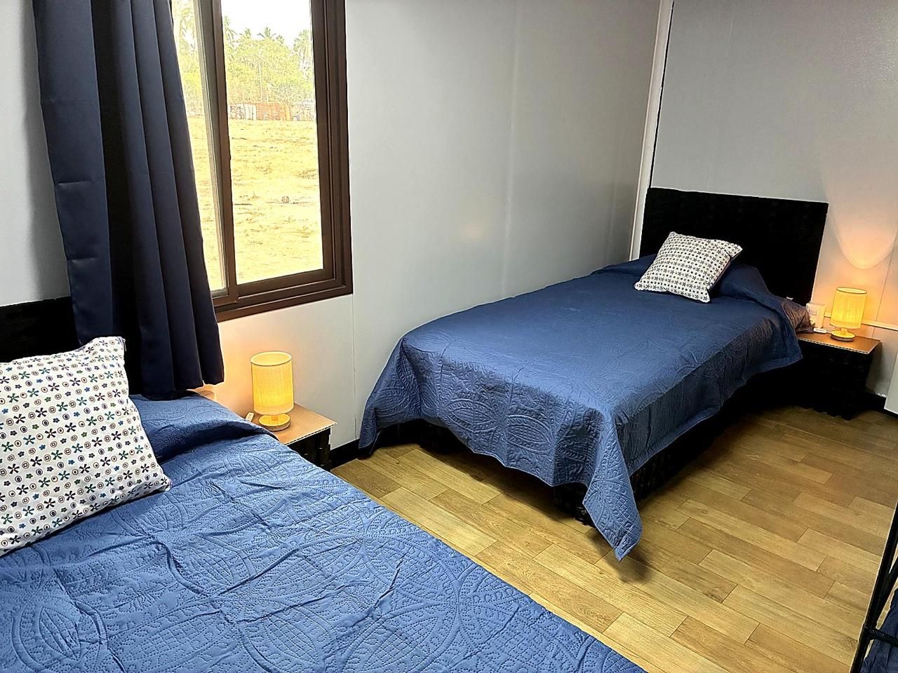 A room with two beds, each with a blue bedspread and a patterned pillow. There are bedside lamps on wooden nightstands.