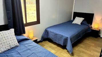 A room with two beds, each with a blue bedspread and a patterned pillow. There are bedside lamps on wooden nightstands.