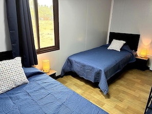 Una habitación con dos camas, cada una con cubrecama azul y almohada estampada. Hay lámparas de noche sobre mesitas de madera.