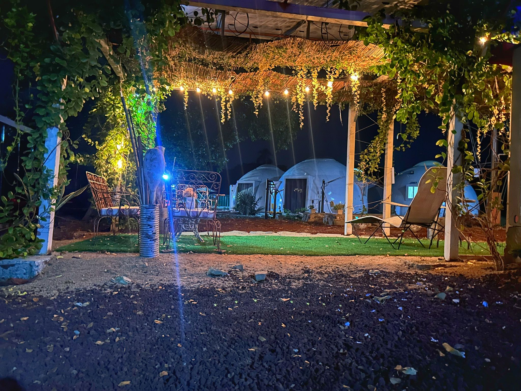 A covered outdoor area with string lights, a pergola, and a seating area with chairs.
