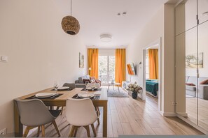 Un comedor moderno con una mesa de madera preparada para dos personas, un sofá y vistas al exterior a través de grandes ventanales.