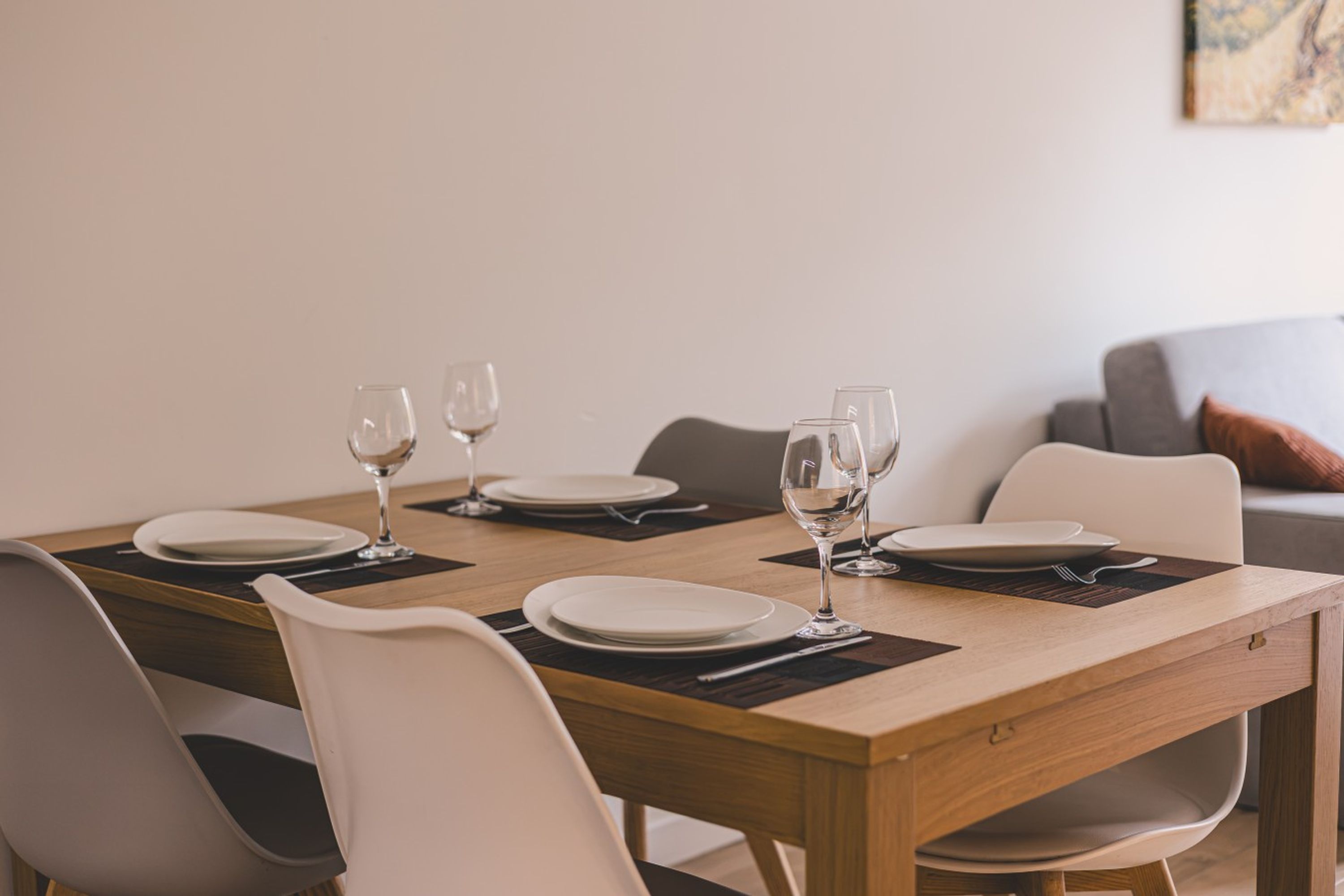 Una mesa de comedor dispuesta con platos, vasos y cubiertos, rodeada de sillas.