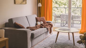 A modern living room with a grey sofa, a round coffee table, and a view of outdoor furniture through large windows.