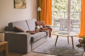 A modern living room with a grey sofa, a round coffee table, and a view of outdoor furniture through large windows.