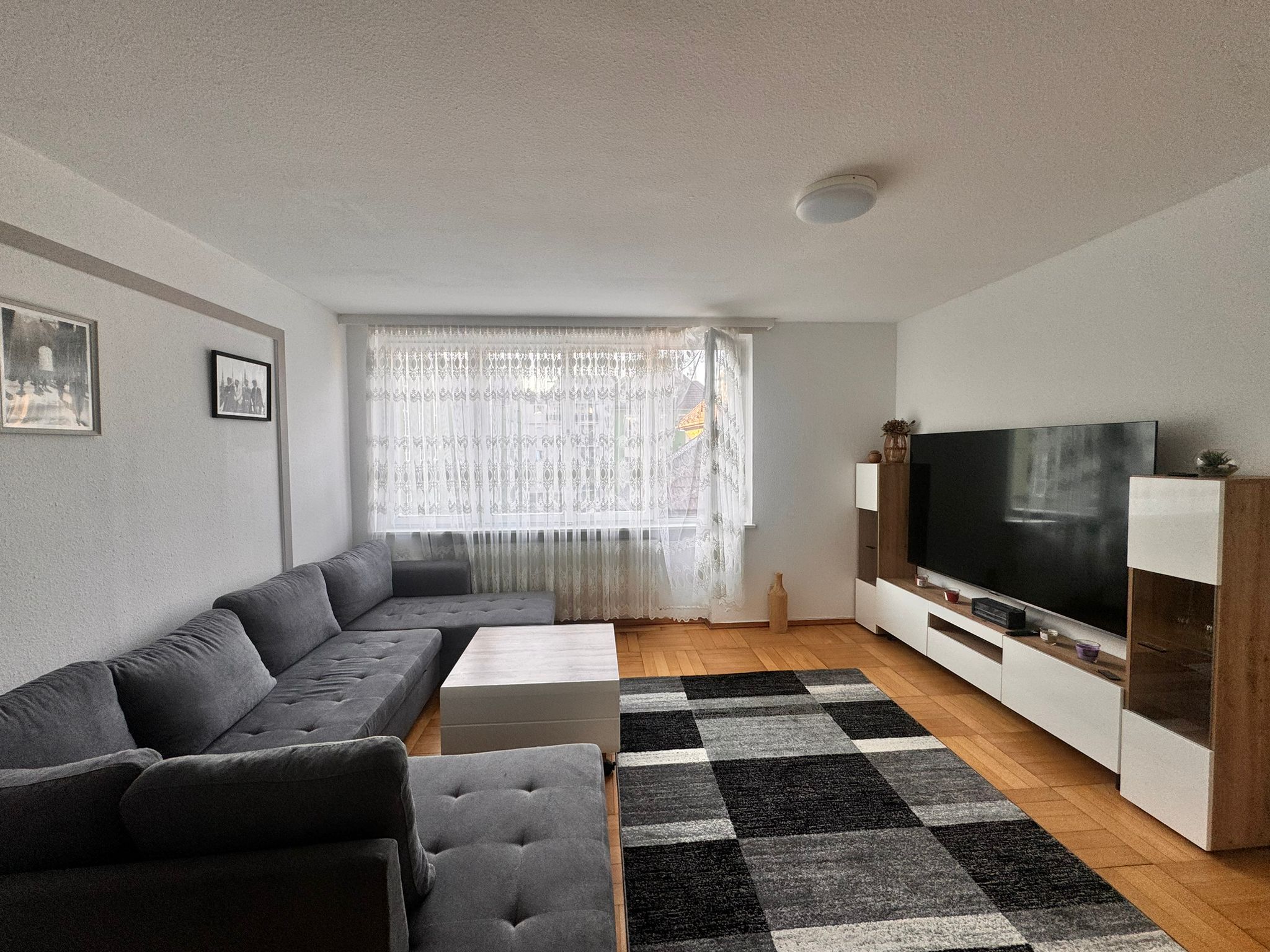 A modern living room with a sectional sofa, a flat-screen TV, and a patterned rug.
