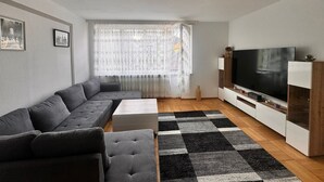 A modern living room with a sectional sofa, a flat-screen TV, and a patterned rug. - E&H Appartements  (Bregenz)
