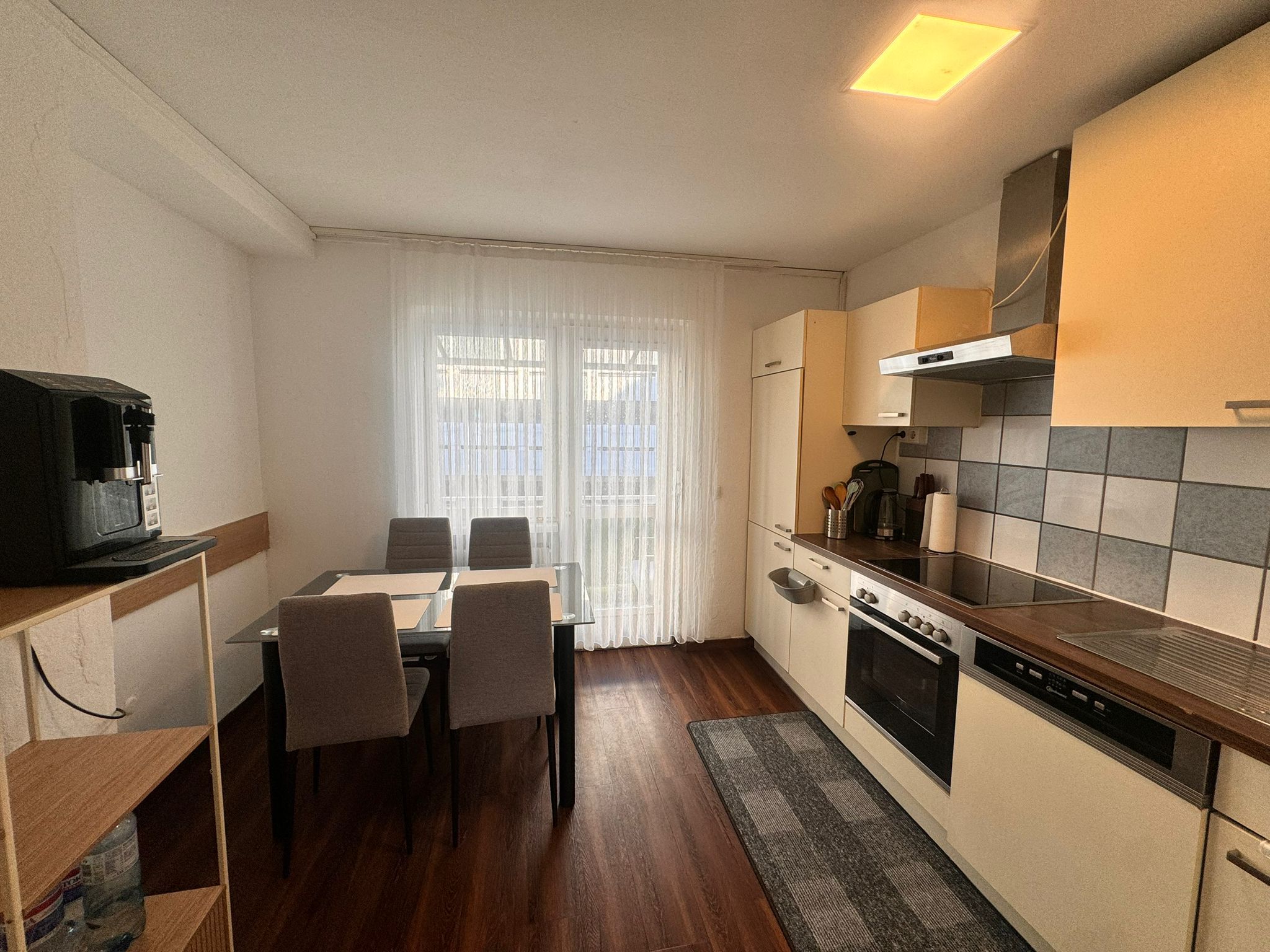 A compact kitchen with a dining table, chairs, a coffee machine, and a stove.