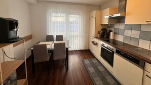 A compact kitchen with a dining table, chairs, a coffee machine, and a stove. - E&H Appartements  (Bregenz)